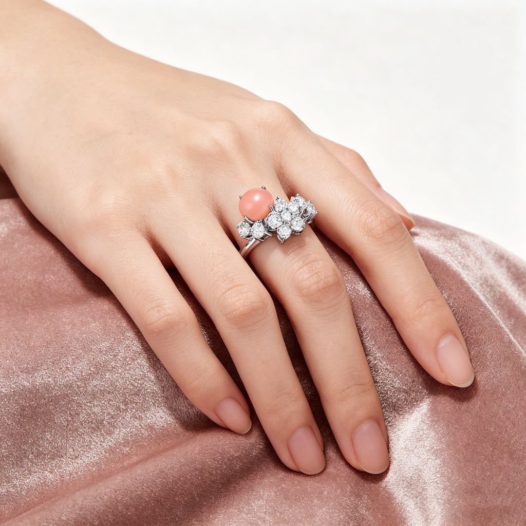 Hand wearing TASA 18K white gold natural pink conch pearl ring with diamond cluster setting, on pink satin background
